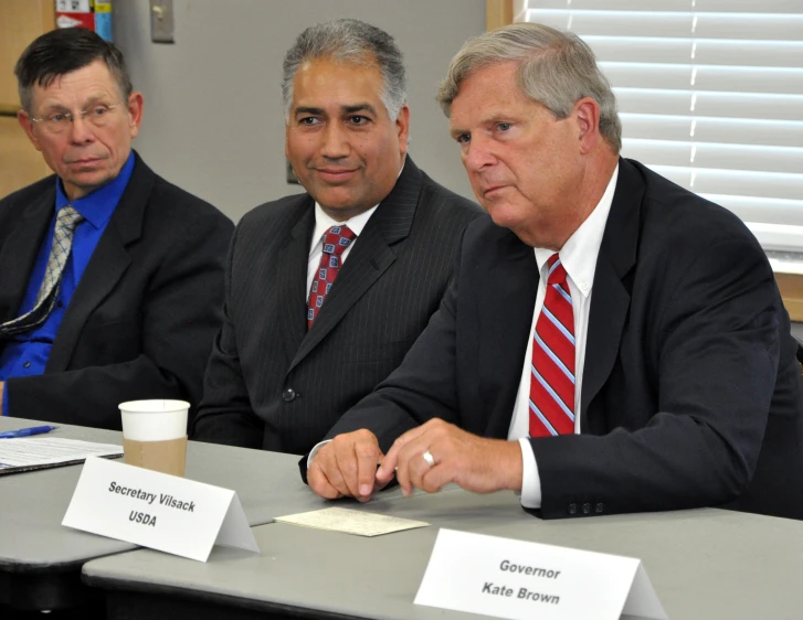 three men in suits and ties at a table looking down