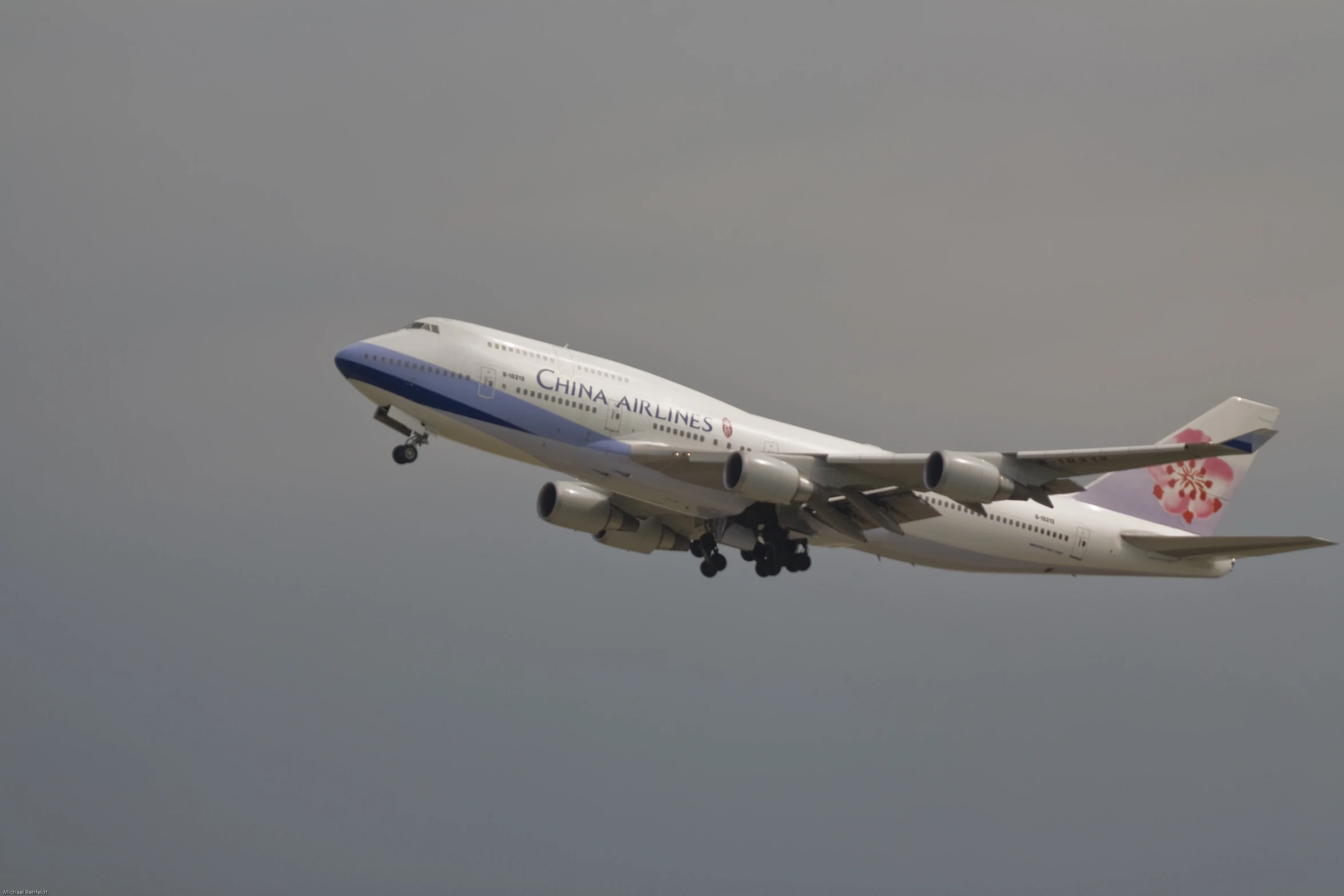 an airplane flying through the grey sky with its wheels down