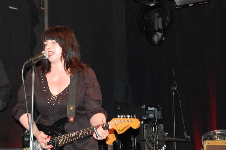 a woman in a black top playing guitar and singing into a microphone