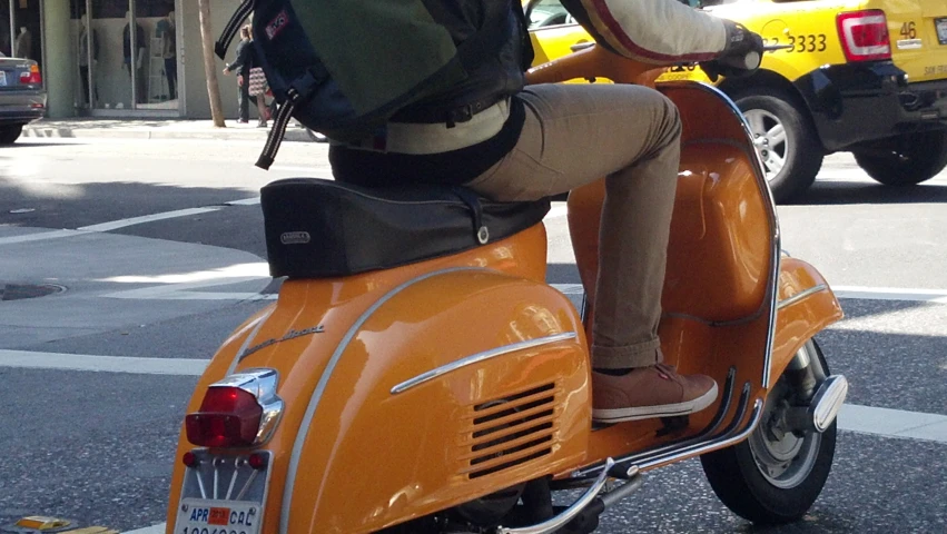 person riding orange scooter in city intersection with yellow taxi