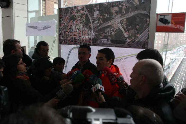 a man in an orange jacket is surrounded by reporters