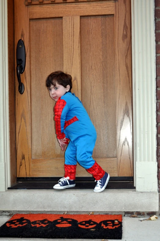 a boy in a spider - man suit, standing at the door