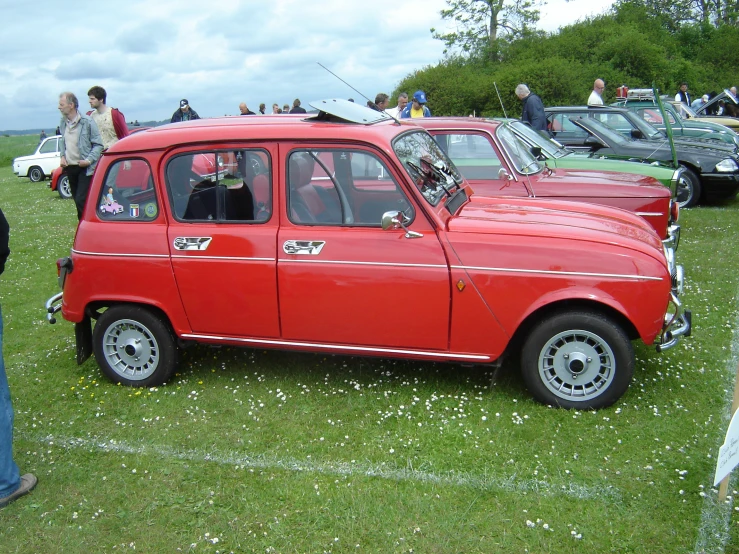 a small red car with several people standing around it