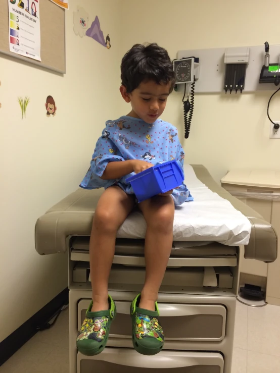 a small child sits on the back of a hospital bed with green shoes