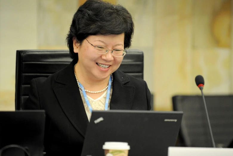 an asian woman is smiling and talking on her laptop