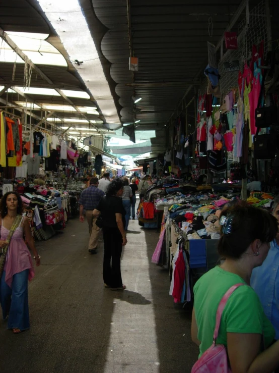 people walk through a market, which is lined with stalls filled with clothes