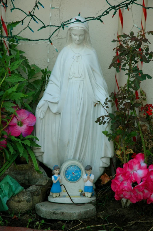 a statue of the virgin mary sits in a flower bed