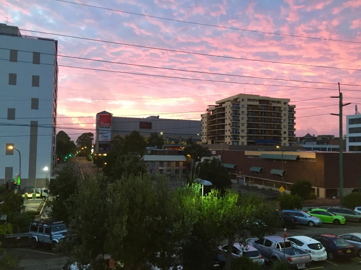 an orange sunset in the city with cars parked in the lot and a tall building