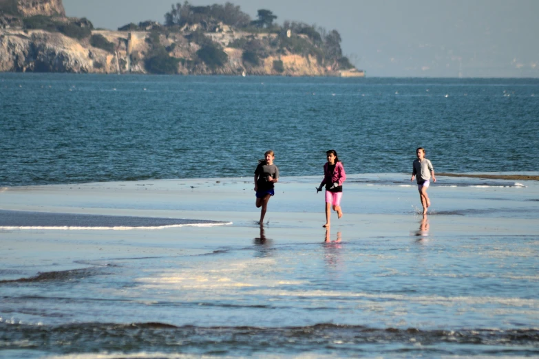 four women walk along a beach while a small island sits above them