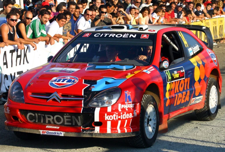 a red car with an american flag painted on it drives past a crowd of spectators