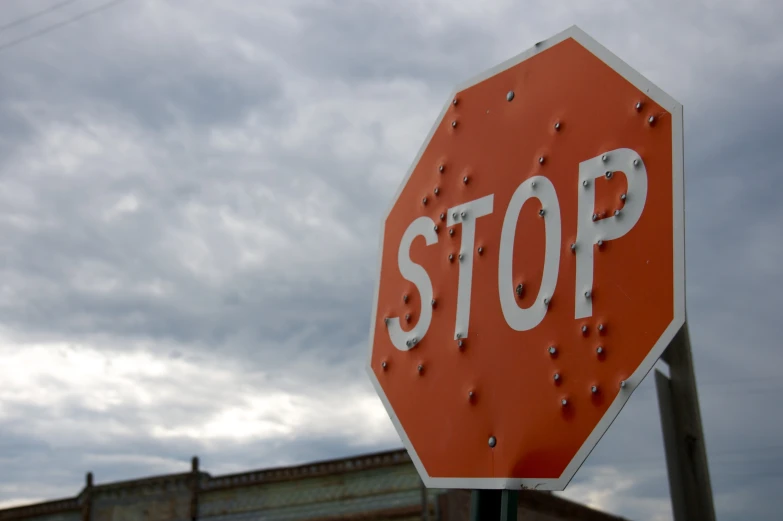 a stop sign with rivets is in front of a gray sky