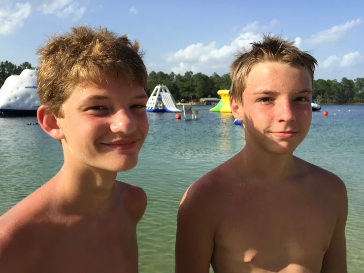 two boy standing next to each other in front of a lake