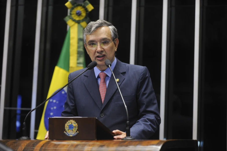 a man in suit speaking in front of several flags