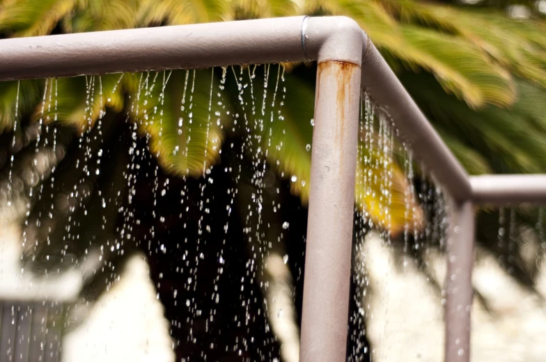 rain falling down on a metal railing that is surrounded by trees