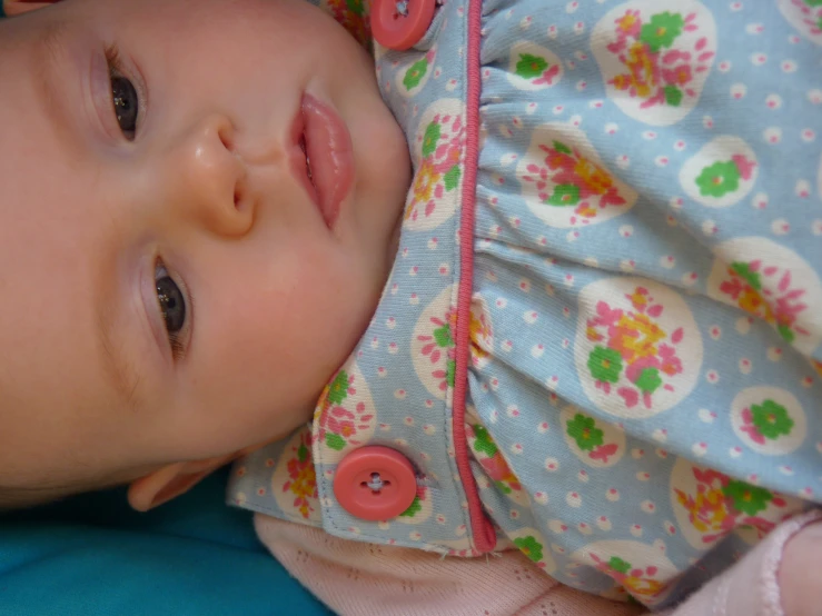 a baby in a dress sitting on a blue chair