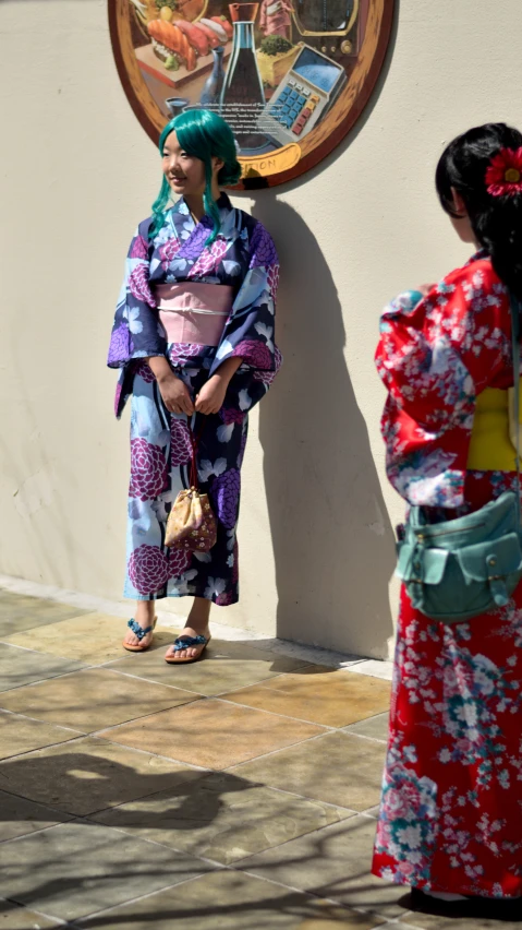 two geisha women stand against a wall in traditional asian clothing