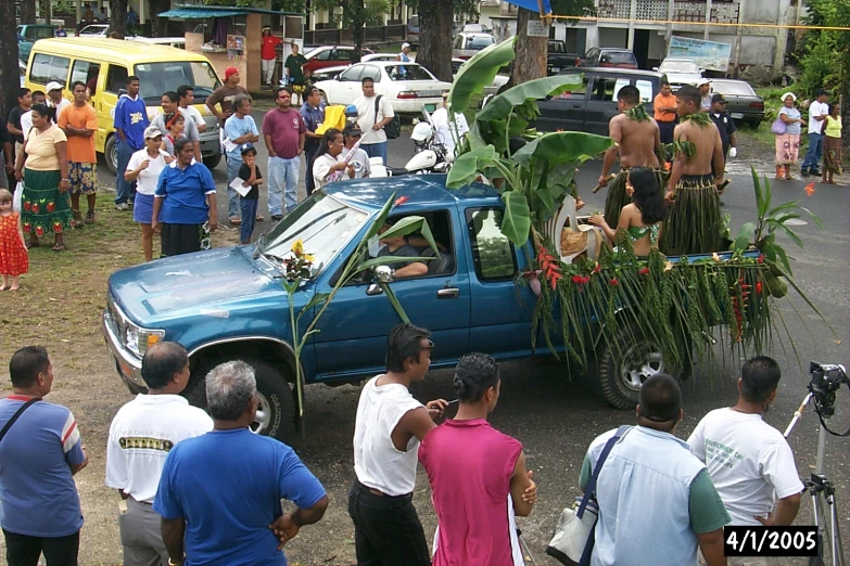 several people looking at a truck with fruit on the back