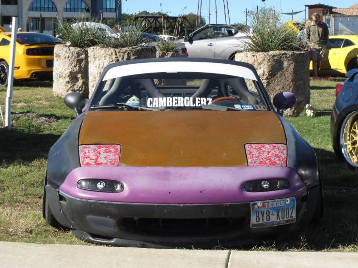 an old pink and purple car sitting on top of grass