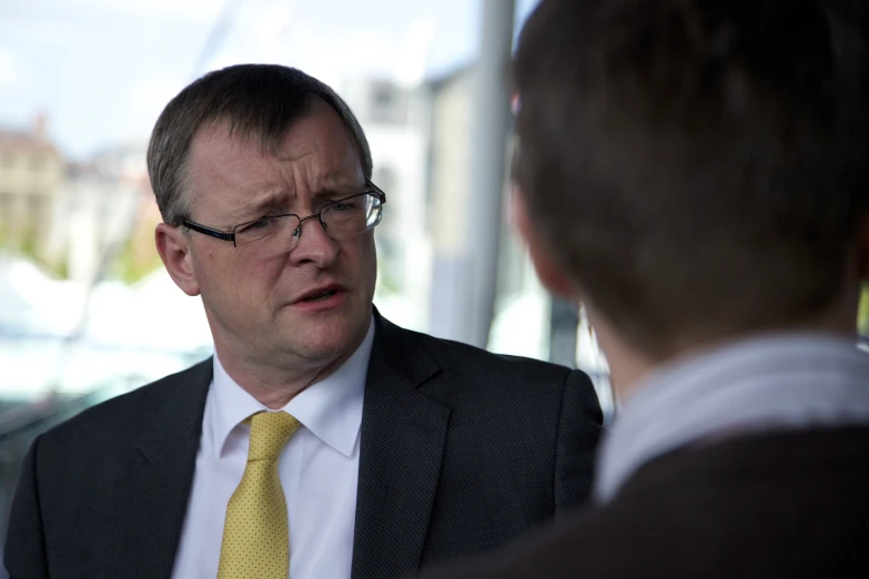 a man talking to another person wearing a suit