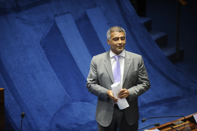 an older man in a suit stands and holds papers