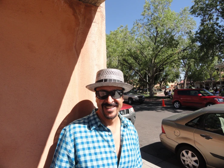 man wearing sunglasses and a hat leaning on a wall
