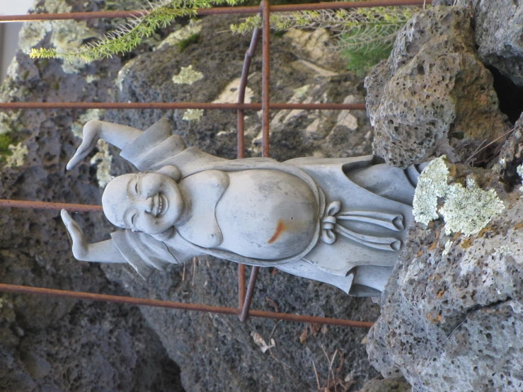 a small statue in front of a rock and iron gate