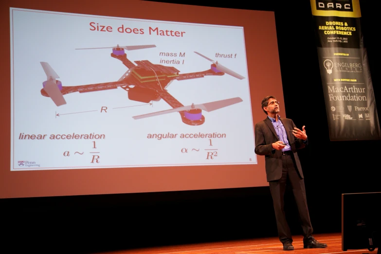 a man speaking at a lecture with two screens in front of him