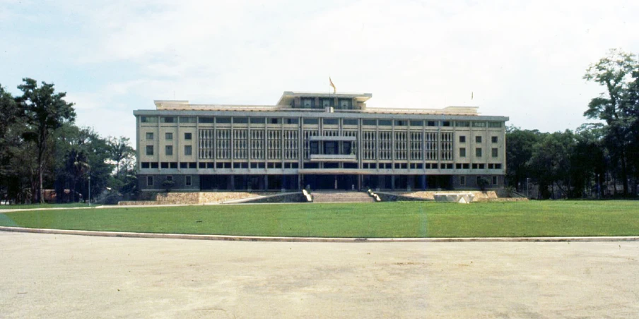 the view from across a paved area shows an old stone building and green grass