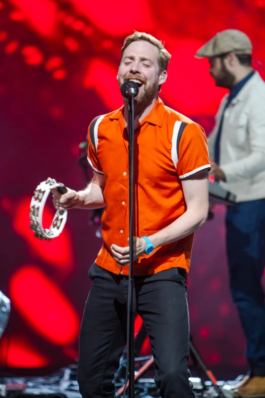 a man in orange shirt singing on stage