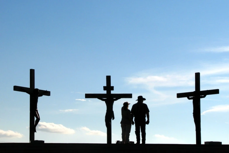 three people in silhouette near three crosses on the mountain