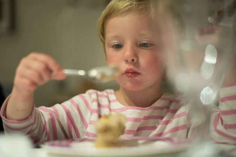 young child sitting at table eating food in glass bowl