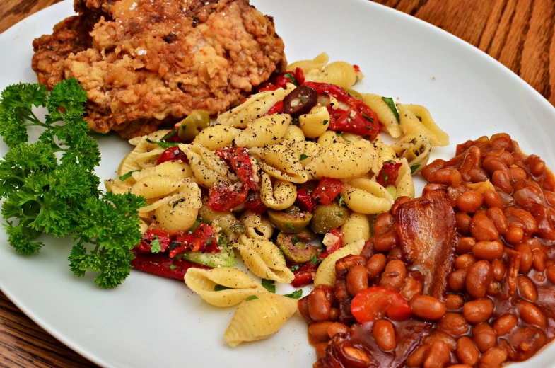 a plate of pasta, beans, a fried chicken and some greens