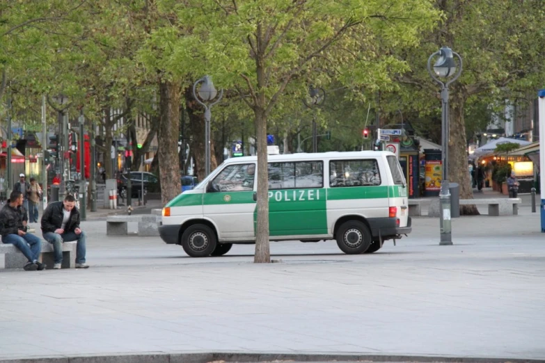 a small green and white van sits on the corner near the park