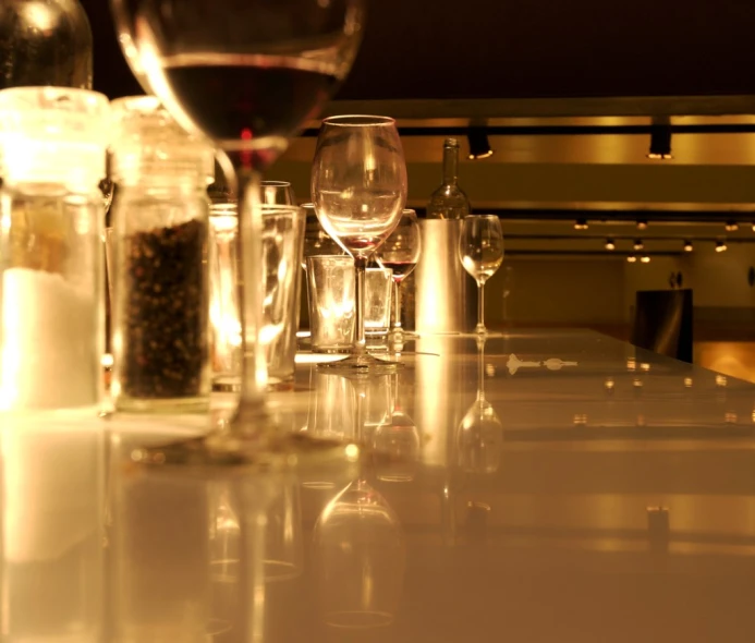wine glasses on a long counter next to a few empty bottles