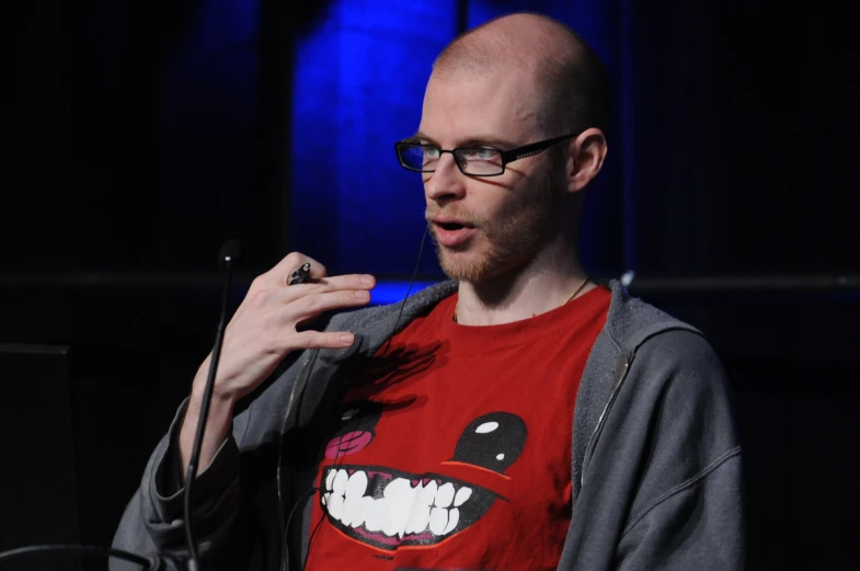 a man with glasses and a shirt on talking to a microphone