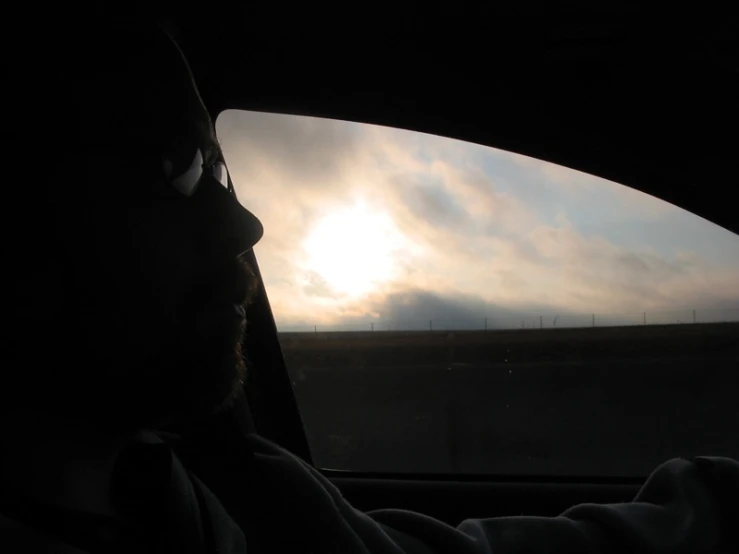 a man drives his car toward the sunset