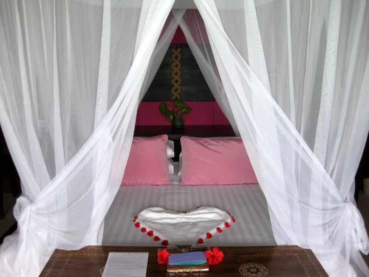 a bed with two white curtains and a pink bed cover