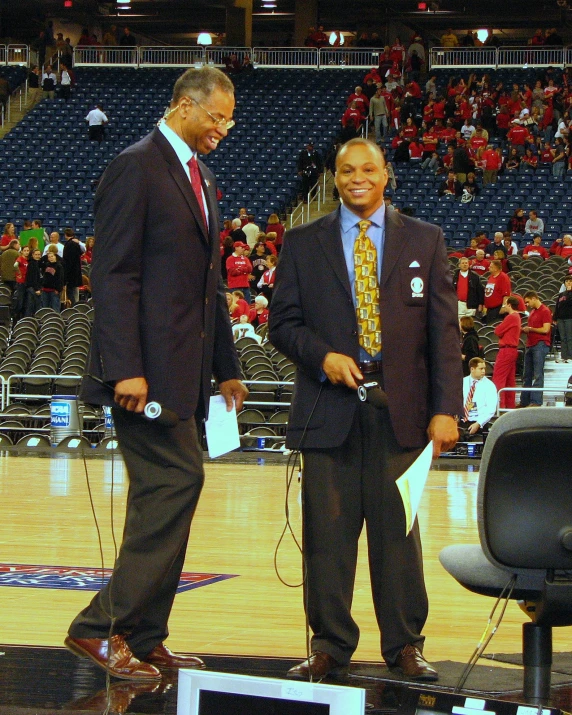 two men in business suits and ties standing at the basketball court