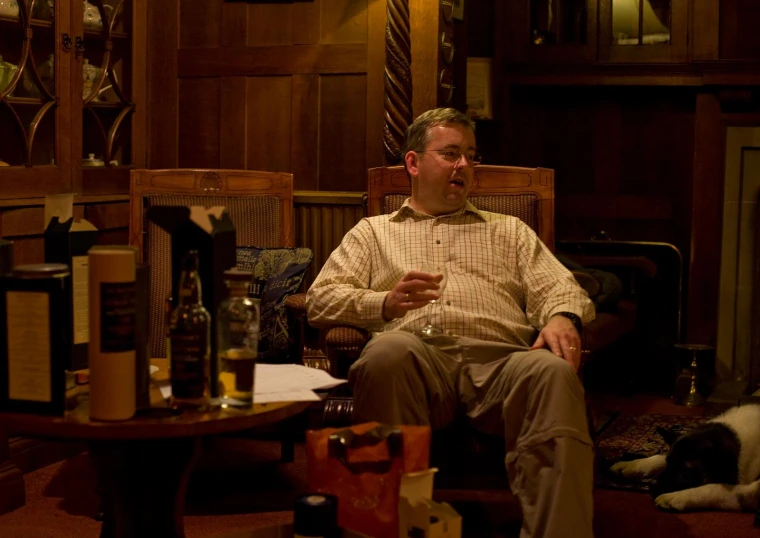 an older man sitting in a chair with a bottle of wine