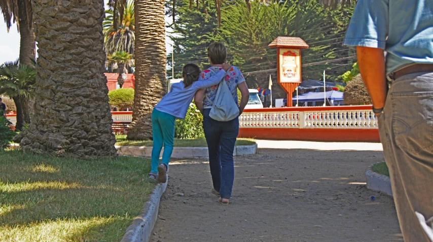 the woman and child are walking down a sidewalk near palm trees