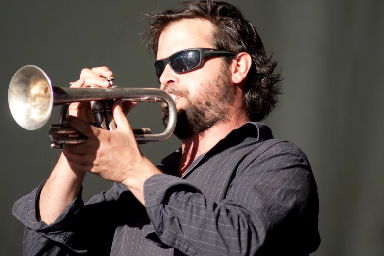 a man in sunglasses plays a trumpet at a music festival