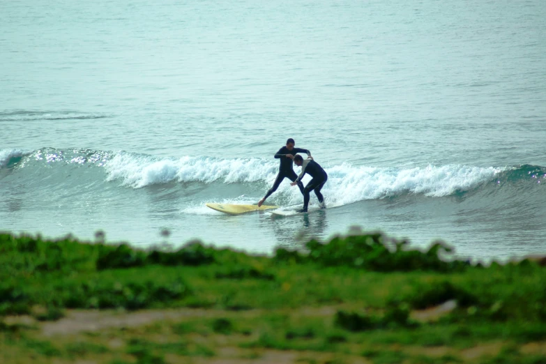 two people in black wet suits riding surfboards