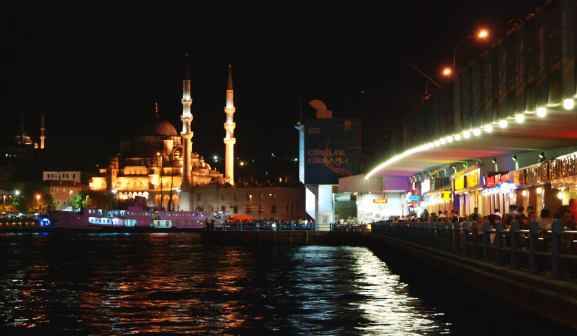 several people are walking on a pier by the water at night