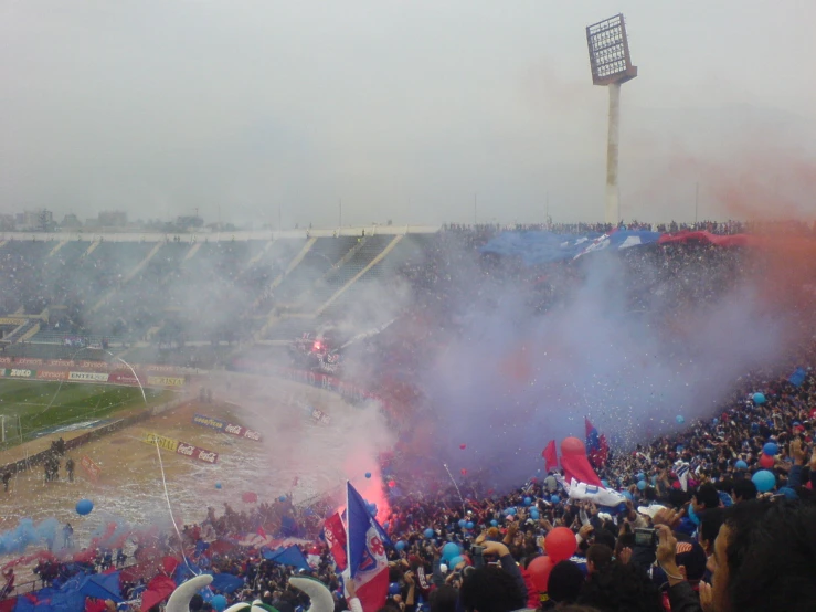 fans gathered outside an empty stadium as smoke rises in the air