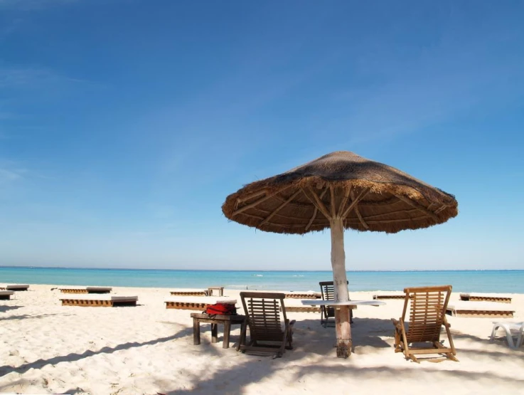 an empty beach with chairs, umbrella and table in the sand