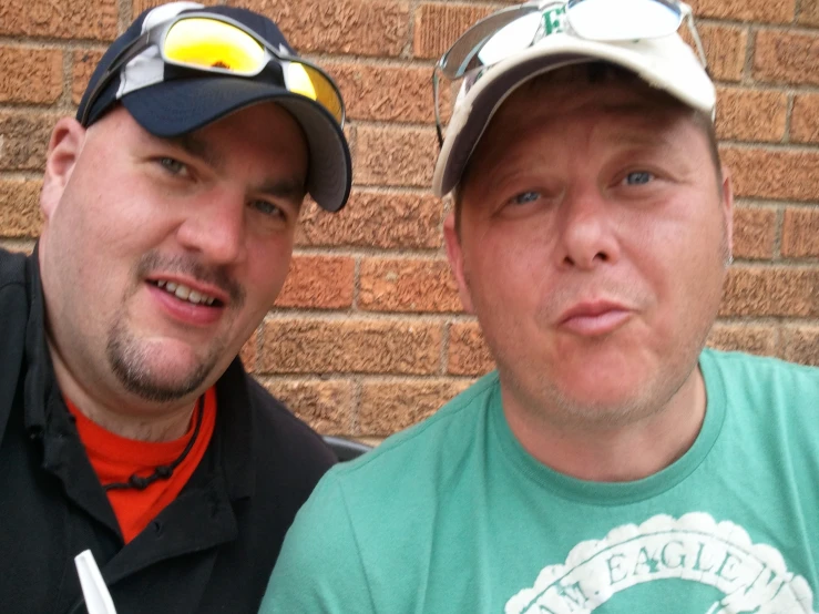 two men with sun glasses standing next to a brick wall