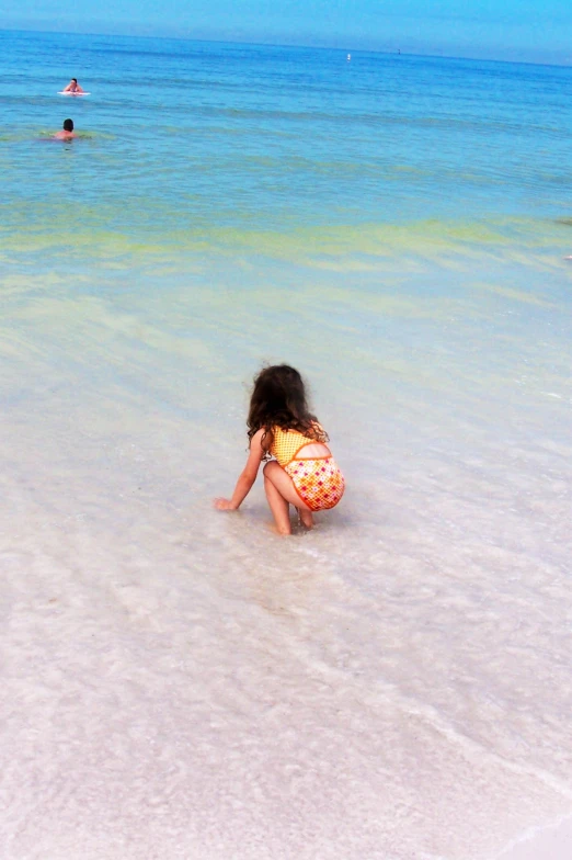 little girl playing in clear ocean waters with other swimmers