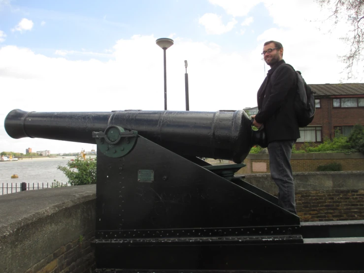 a man looks at a large cannon near a lake