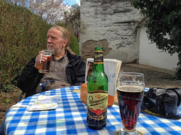 two men sitting at an outdoor table with beer bottles