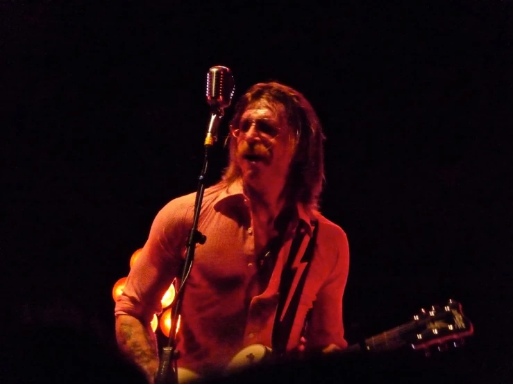 a shirtless man playing a guitar in front of a microphone